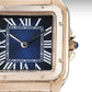 Rose gold watch with blue face and Roman numerals on a gray background